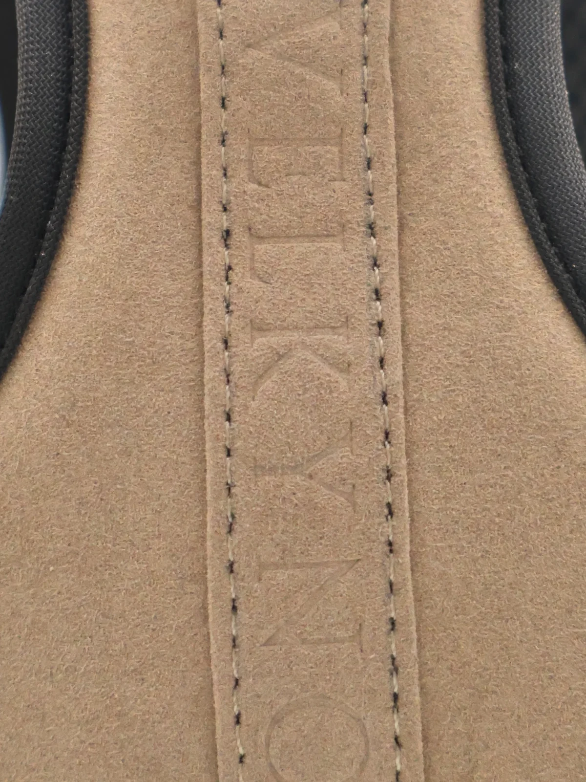 Macro of the taupe suede-touch microfiber, with the embossed VELKYNO and its stitching