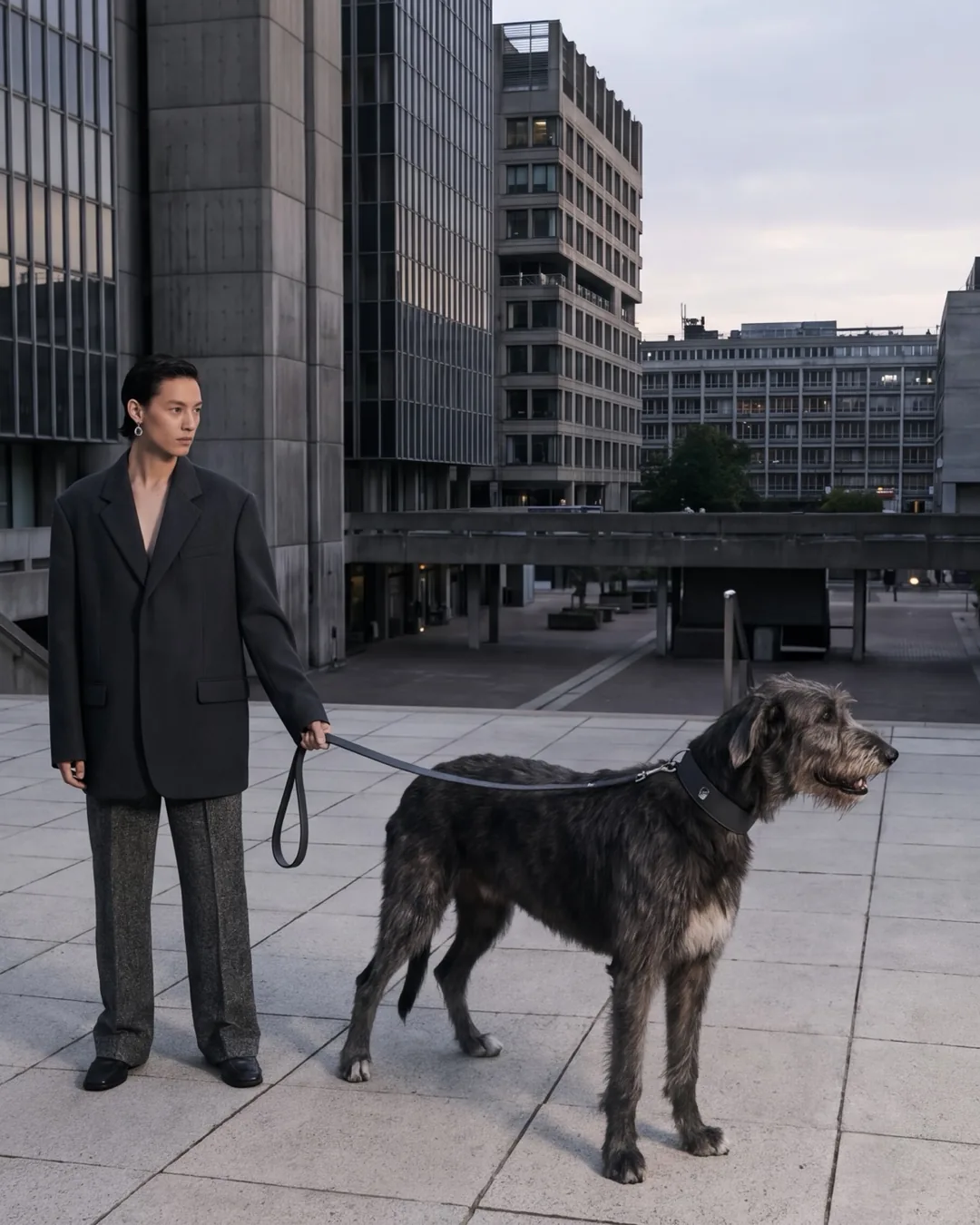 Man in a graphite coat walking an Irish Wolfhound through concrete architecture